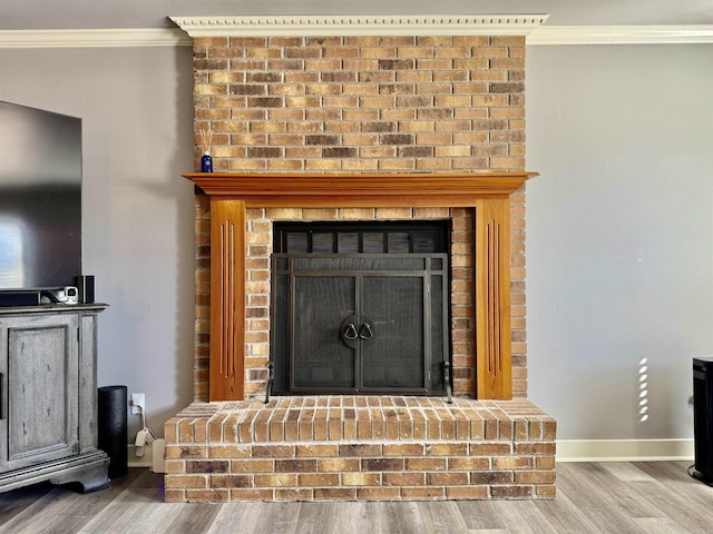 room details featuring a brick fireplace, wood finished floors, baseboards, and ornamental molding