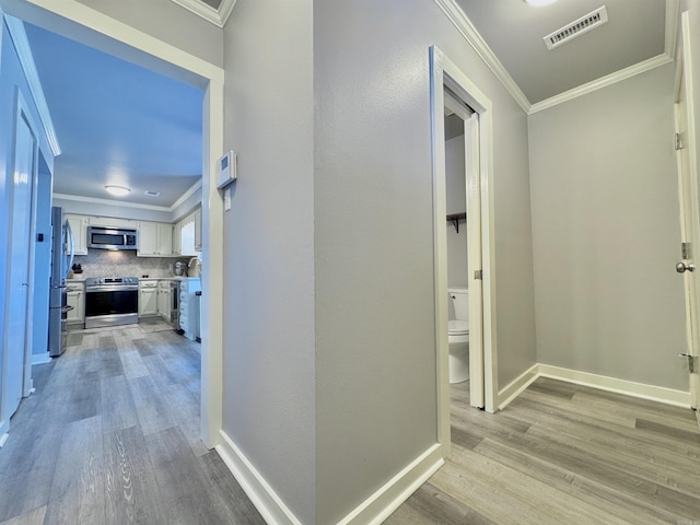 corridor featuring visible vents, light wood-style floors, and ornamental molding