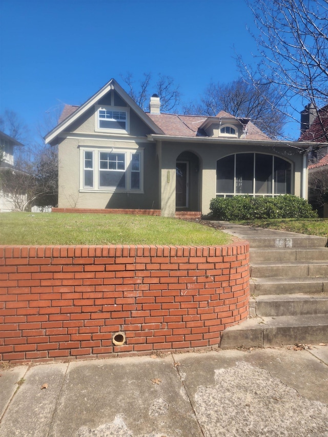 view of front facade with a front yard, a chimney, and stucco siding