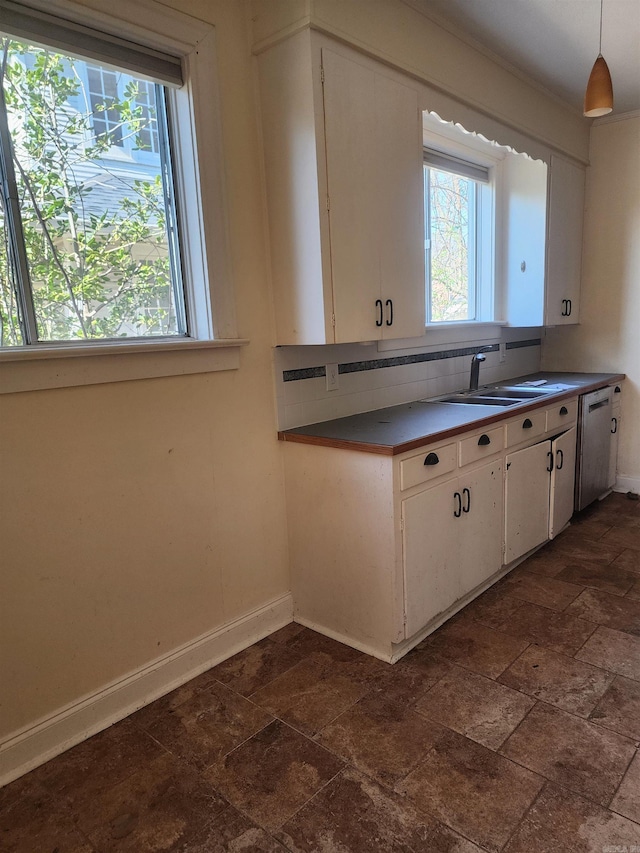 kitchen with backsplash, baseboards, dishwasher, white cabinets, and a sink