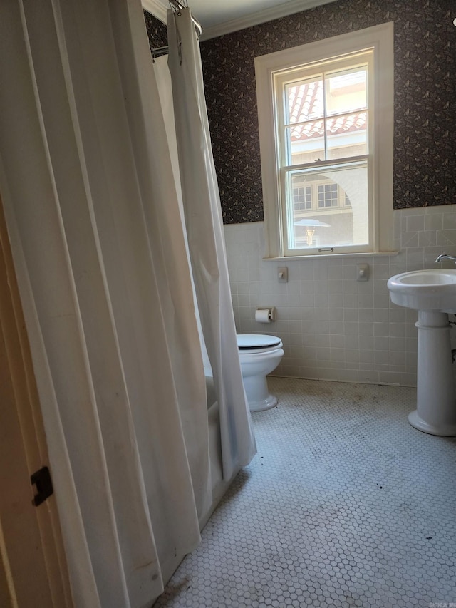 bathroom with wallpapered walls, tile walls, toilet, and a wainscoted wall