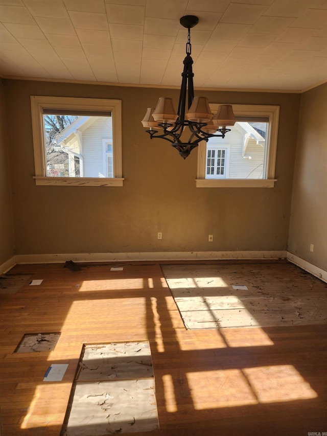 unfurnished dining area featuring a notable chandelier, wood finished floors, and baseboards