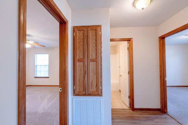 hall featuring light colored carpet, visible vents, and baseboards