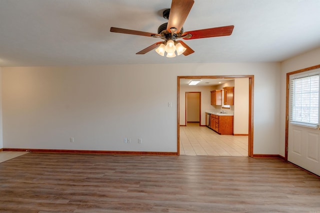 empty room with a ceiling fan, baseboards, light wood-type flooring, and a sink