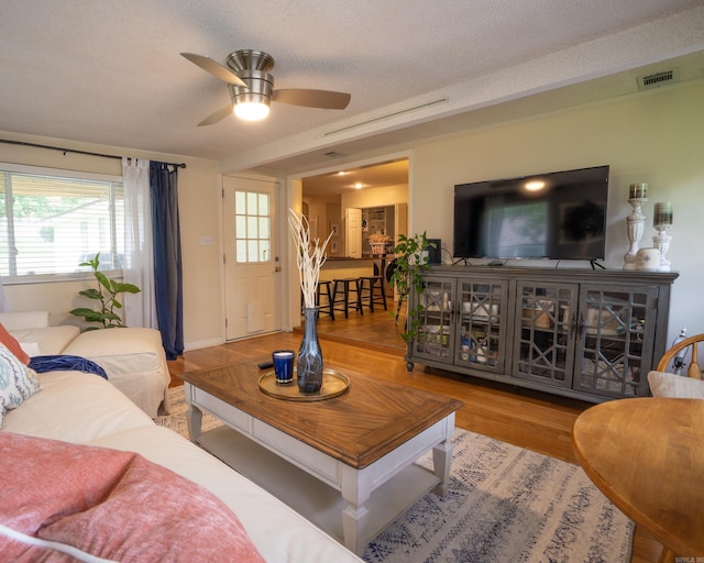 living area with visible vents, a textured ceiling, a ceiling fan, and wood finished floors