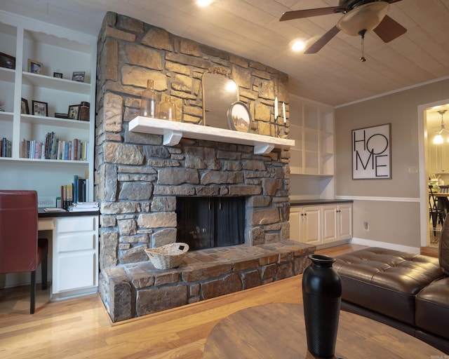 living room with built in study area, light wood-style flooring, a stone fireplace, wood ceiling, and crown molding