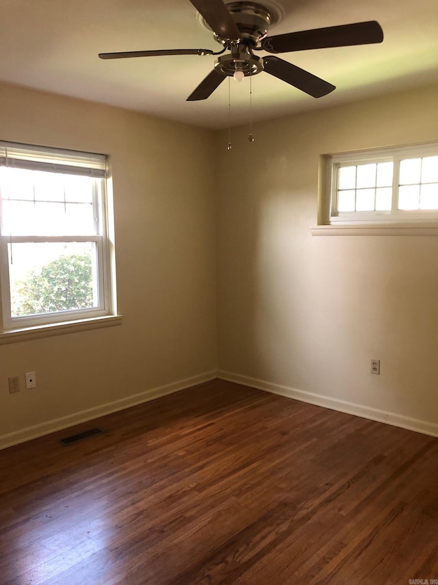 unfurnished room with a ceiling fan, visible vents, dark wood-style flooring, and baseboards