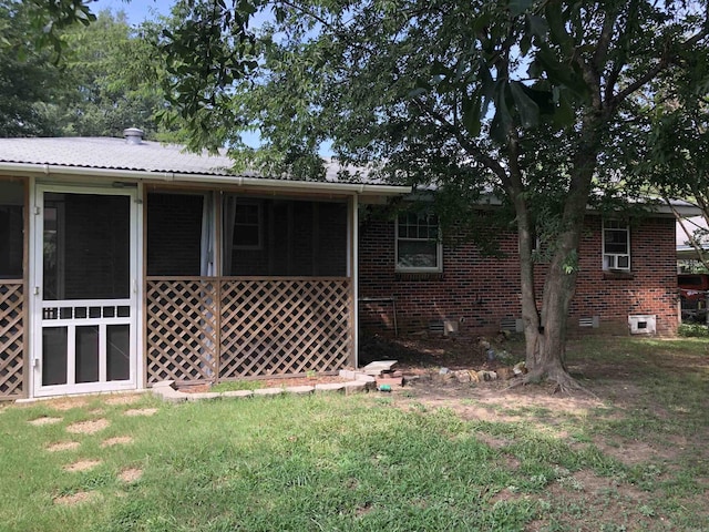 view of side of home with crawl space, brick siding, a lawn, and a sunroom