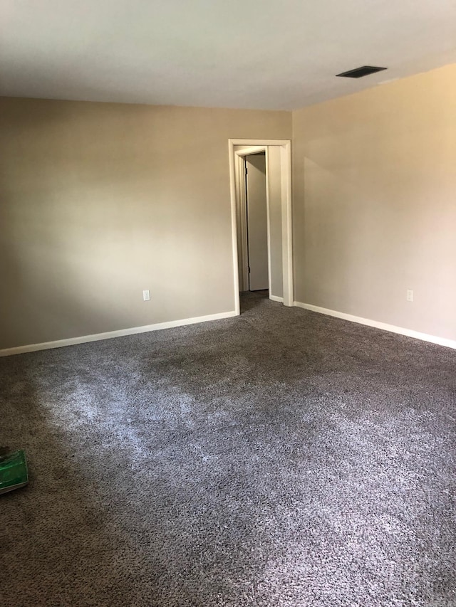 spare room featuring visible vents, baseboards, and dark colored carpet