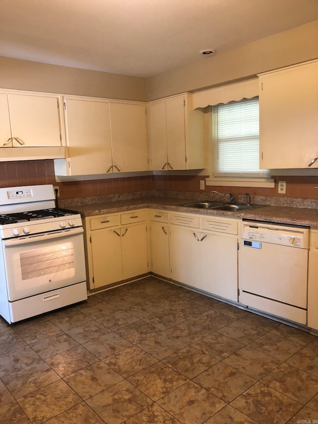 kitchen with white appliances, a sink, under cabinet range hood, dark countertops, and tasteful backsplash