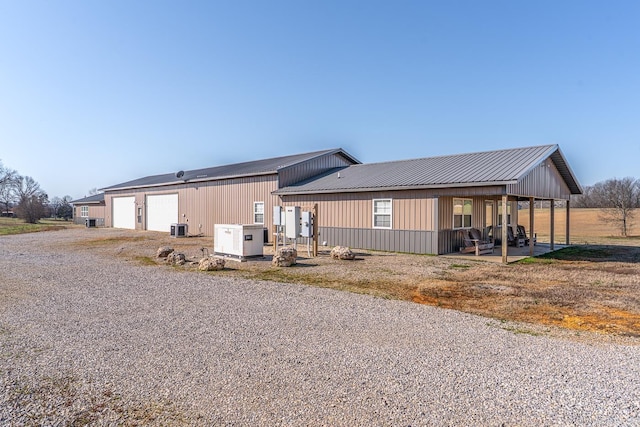 view of front facade with central AC unit, metal roof, gravel driveway, and a garage