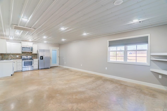 kitchen with a sink, finished concrete floors, appliances with stainless steel finishes, white cabinets, and baseboards