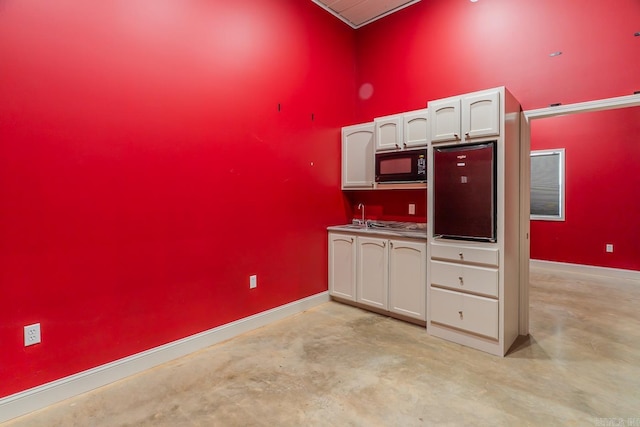 kitchen with white cabinetry, concrete floors, black microwave, and a sink