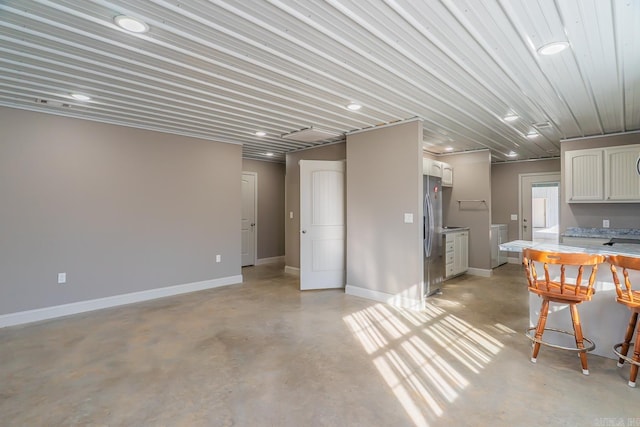 kitchen featuring concrete floors, baseboards, washer and clothes dryer, white cabinets, and stainless steel fridge