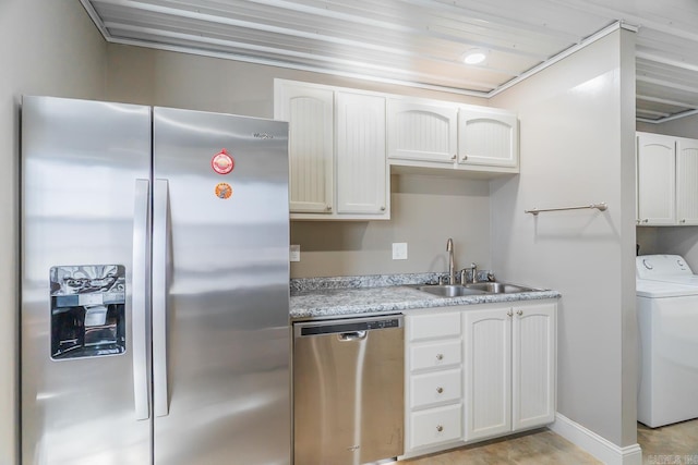 kitchen with washer / dryer, a sink, light countertops, appliances with stainless steel finishes, and white cabinetry