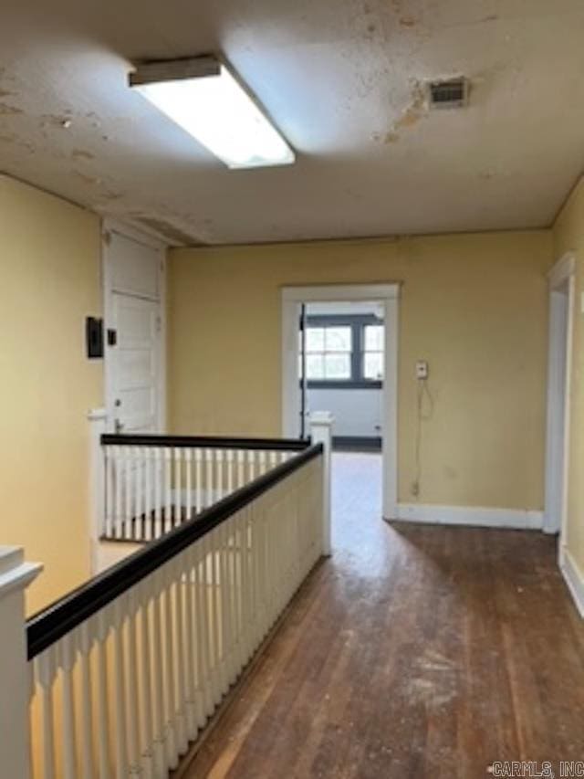 hallway with baseboards, visible vents, and wood finished floors