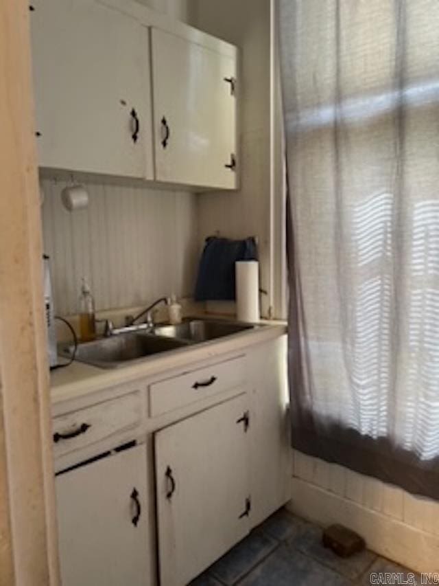 kitchen featuring dark tile patterned floors, white cabinets, light countertops, and a sink