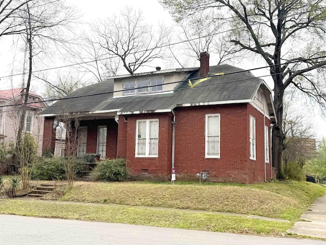 view of front of property featuring roof with shingles, a chimney, brick siding, a front lawn, and crawl space