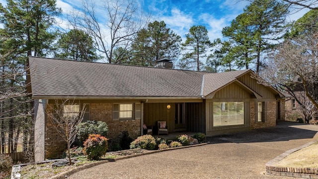 ranch-style house with a shingled roof, covered porch, brick siding, and a chimney