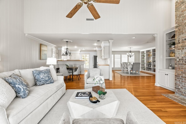 living area with visible vents, light wood-style floors, crown molding, and ceiling fan with notable chandelier