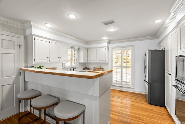 kitchen featuring visible vents, white cabinetry, ornamental molding, stainless steel appliances, and a kitchen bar