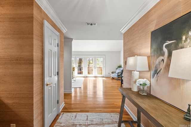 hall featuring wood finished floors, baseboards, visible vents, ornamental molding, and french doors