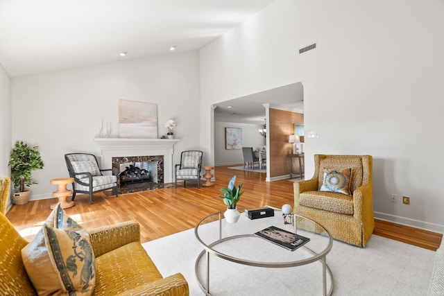 living area with wood finished floors, visible vents, baseboards, high vaulted ceiling, and a high end fireplace