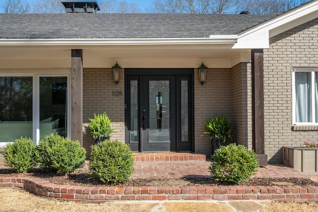 view of exterior entry with brick siding and a shingled roof