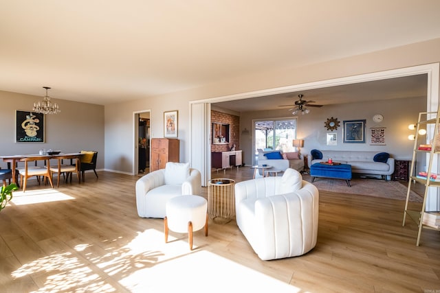 living area with ceiling fan with notable chandelier, baseboards, and light wood finished floors