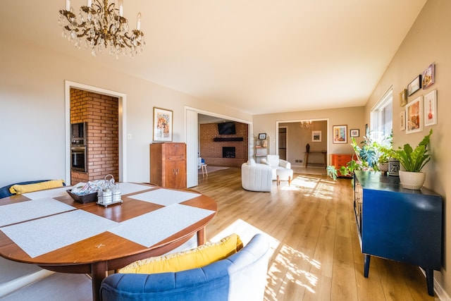 dining space featuring a brick fireplace, a notable chandelier, and light wood-type flooring