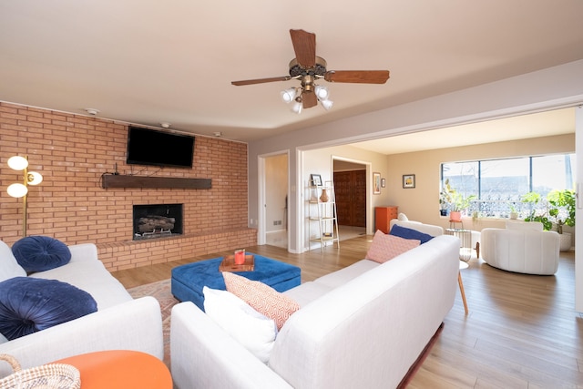 living area with a brick fireplace, light wood-style flooring, a ceiling fan, and brick wall