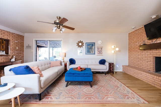 living room with a brick fireplace, ceiling fan, and wood finished floors