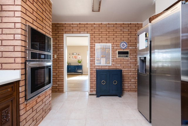 kitchen with light tile patterned floors, appliances with stainless steel finishes, and brick wall