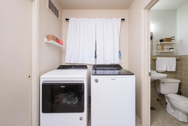 laundry room with a wainscoted wall, visible vents, washing machine and clothes dryer, laundry area, and tile walls