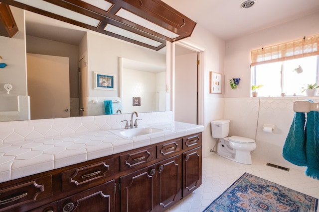 bathroom with visible vents, toilet, vanity, wainscoting, and tile walls