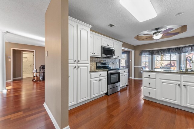 kitchen featuring visible vents, backsplash, appliances with stainless steel finishes, white cabinets, and dark wood-style flooring