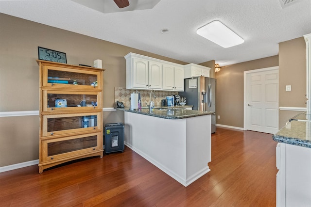 kitchen featuring dark wood-type flooring, white cabinets, dark stone countertops, and stainless steel fridge