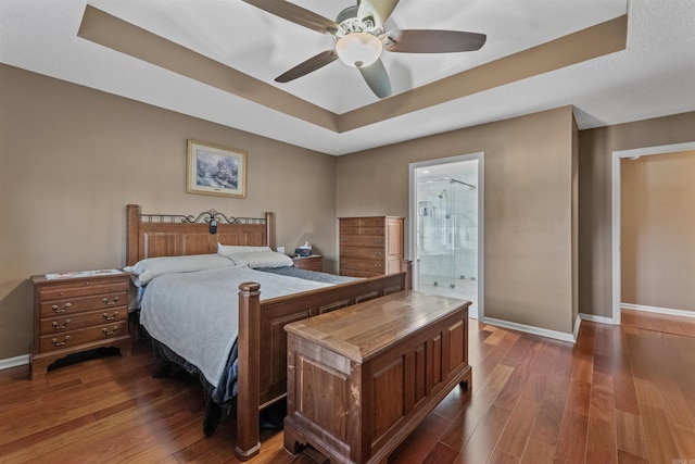 bedroom featuring dark wood finished floors, baseboards, a tray ceiling, and a ceiling fan