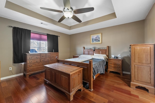 bedroom with visible vents, a raised ceiling, baseboards, and dark wood finished floors