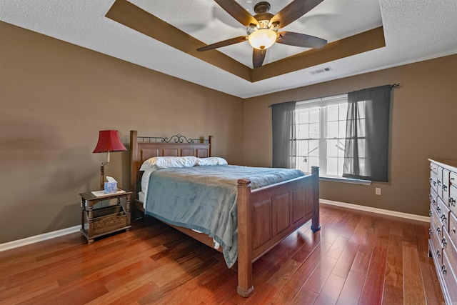 bedroom featuring a tray ceiling, baseboards, visible vents, and wood finished floors