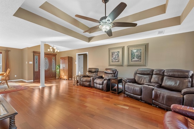 home theater featuring baseboards, visible vents, light wood-style flooring, a raised ceiling, and ceiling fan with notable chandelier