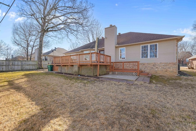 back of house featuring fence, a wooden deck, a chimney, a lawn, and brick siding