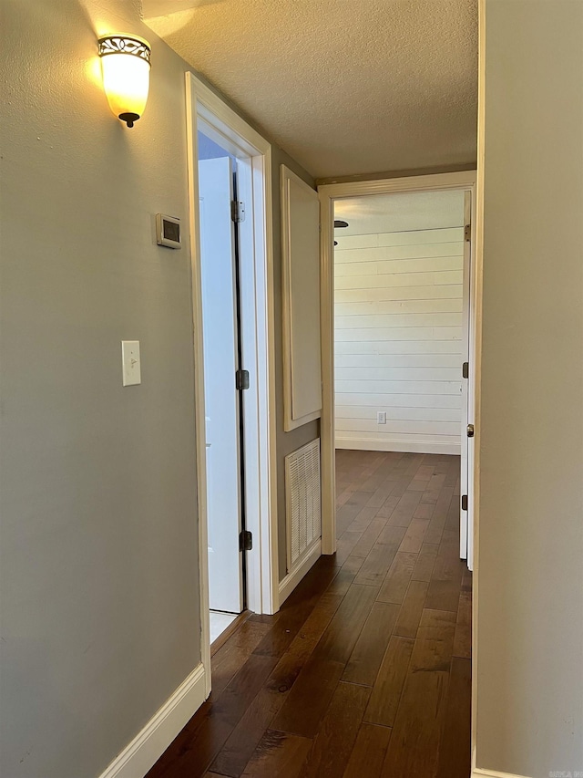 corridor with baseboards, dark wood-style floors, visible vents, and a textured ceiling