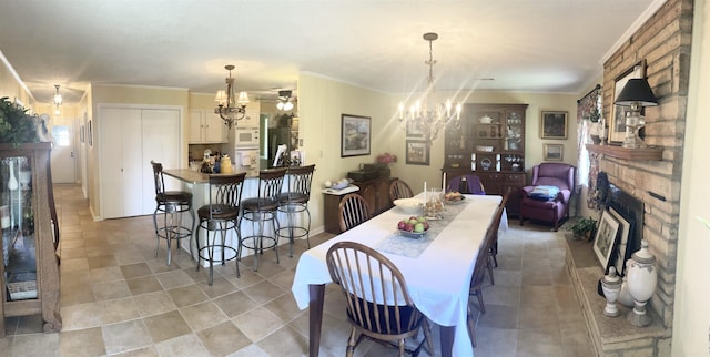 dining space with a brick fireplace, ornamental molding, light tile patterned flooring, and ceiling fan with notable chandelier