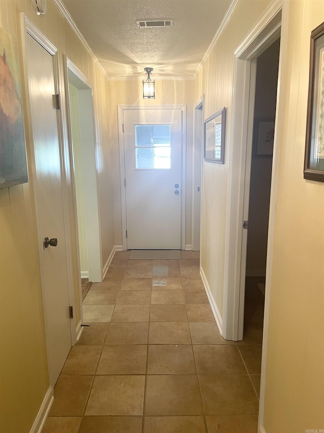 hallway featuring tile patterned floors, visible vents, a textured ceiling, and crown molding