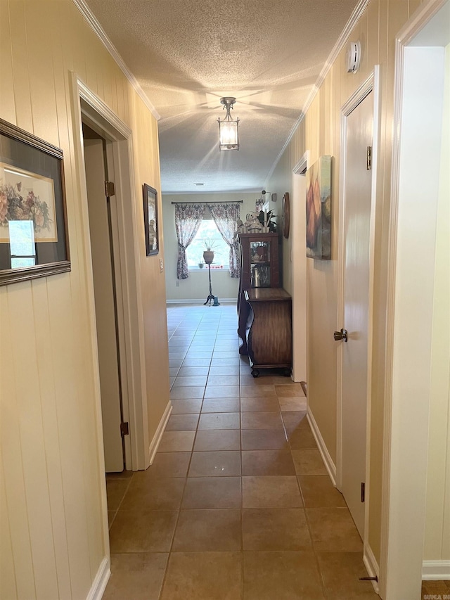 corridor featuring tile patterned flooring, wood walls, a textured ceiling, and ornamental molding