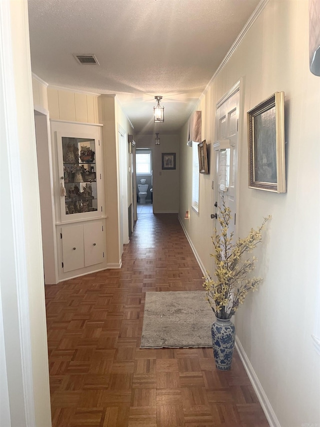 hall featuring visible vents, baseboards, a textured ceiling, and crown molding