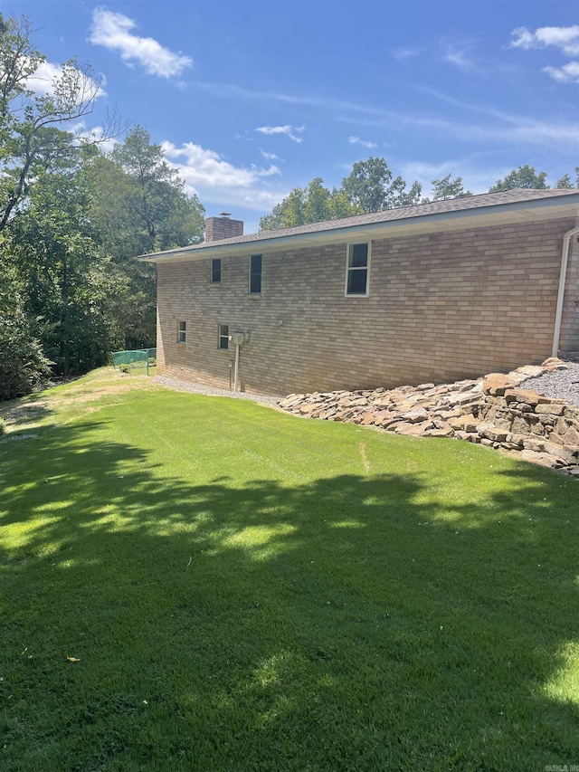 exterior space featuring brick siding, a lawn, and a chimney