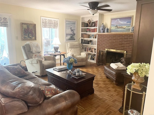 living room with crown molding, built in shelves, a fireplace, and ceiling fan