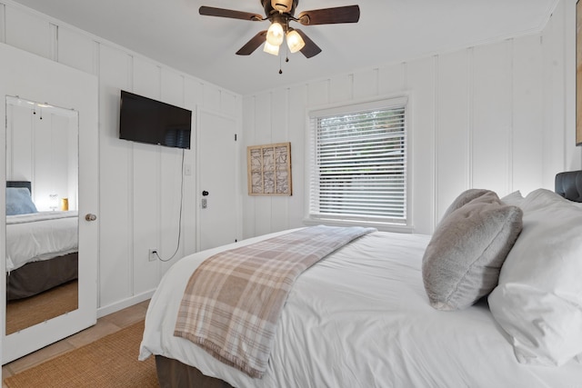 bedroom with a decorative wall, light tile patterned flooring, and a ceiling fan